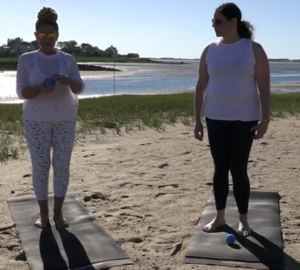 Instructor Sabrina Vaz and Dr. Jessica Pizano stand on yoga mats laying on a beach.